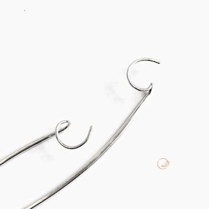 May include: Two silver-colored metal hooks with curved ends. Each hook features a long, slender, slightly arched shaft that terminates in a circular loop. The metallic surface is smooth and reflective, showing a consistent silver tone throughout.
