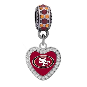 Op de afbeelding: Zilveren bedel met een rood hart met het logo van de San Francisco 49ers. Het hart is omgeven door heldere strass steentjes. De bedel heeft een zilveren kraal met rode en oranje strass steentjes.
