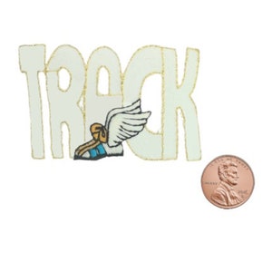 May include: A cream-colored, die-cut word "TRACK" with gold trim, featuring a winged running shoe. A penny is included for size reference. The design is on a white background.