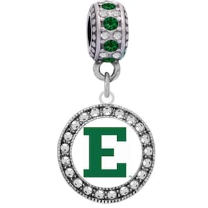 Puede incluir: Un charm plateado con un fondo blanco y una letra "E" verde en el centro. El charm está rodeado por un círculo de cristales transparentes.