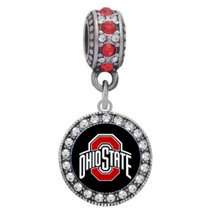 Peut inclure: Breloque argenté avec un logo Ohio State noir et rouge entouré de cristaux transparents. Le charme est attaché à une perle argentée avec des cristaux rouges.