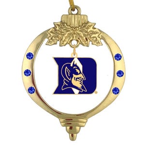 Pode incluir: Adorno de Natal dourado com um logotipo azul e dourado da Duke University com um mascote de diabo azul. O adorno é decorado com strass azuis.