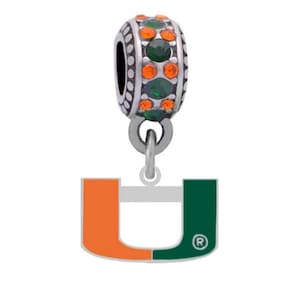 May include: A silver-toned charm bead featuring alternating rows of orange and green circular crystals. Attached to the bead is a dangling U-shaped pendant split into orange and green sections with a registered trademark symbol in the lower right corner.