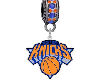Może przedstawiać: Srebrny charm z niebieskimi i pomarańczowymi kryształami. Charm przedstawia logo New York Knicks z piłką do koszykówki w środku.