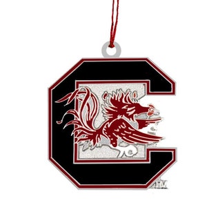 May include: A black and silver Christmas ornament shaped like the letter "C" with a red rooster inside. The ornament has a red ribbon for hanging.