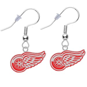 May include: A pair of silver dangle earrings with a red and white Detroit Red Wings logo charm. The logo features a red wing with a white wheel inside.
