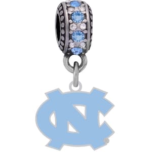 Könnte beinhalten: Ein silberner Anhänger mit einem hellblauen Emaille-Logo der North Carolina Tar Heels. Der Anhänger hat eine silberne Perle mit klaren und hellblauen Kristallen.