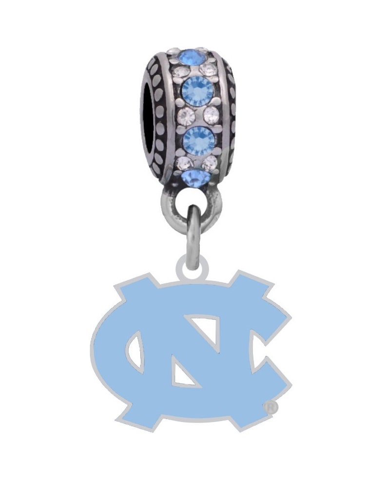 Puede incluir: Un charm plateado con un logotipo de los North Carolina Tar Heels de esmalte azul claro. El charm tiene una cuenta plateada con cristales transparentes y azul claro.