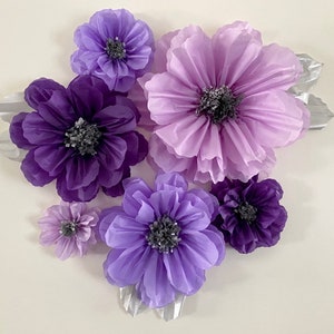 Pode incluir: Um conjunto de sete flores de papel de seda em tons de roxo e lavanda. As flores est&atilde;o dispostas em um cacho e t&ecirc;m uma apar&ecirc;ncia em camadas e com babados.
