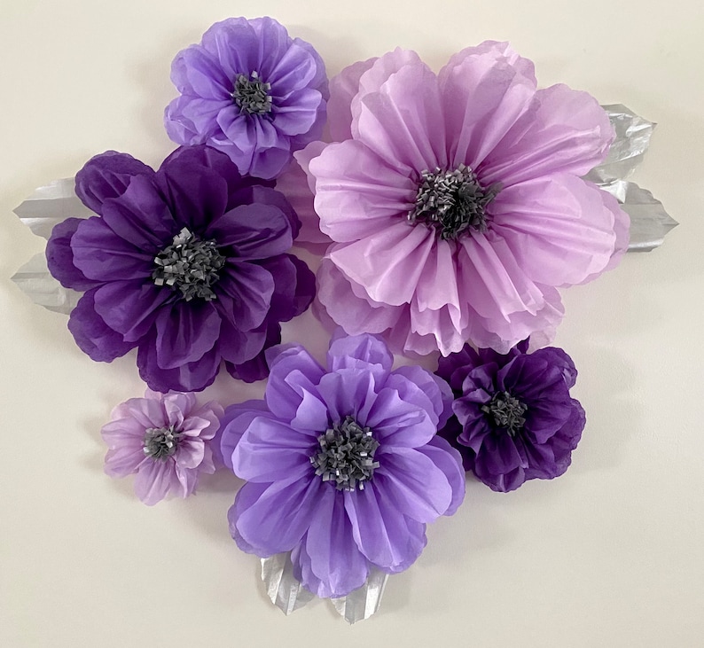 Pode incluir: Um conjunto de sete flores de papel de seda em tons de roxo e lavanda. As flores est&atilde;o dispostas em um cacho e t&ecirc;m uma apar&ecirc;ncia em camadas e com babados.