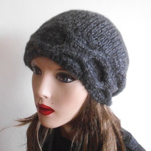 May include: A grey knitted beanie with a unique folded design. The beanie is made from a soft, textured yarn.