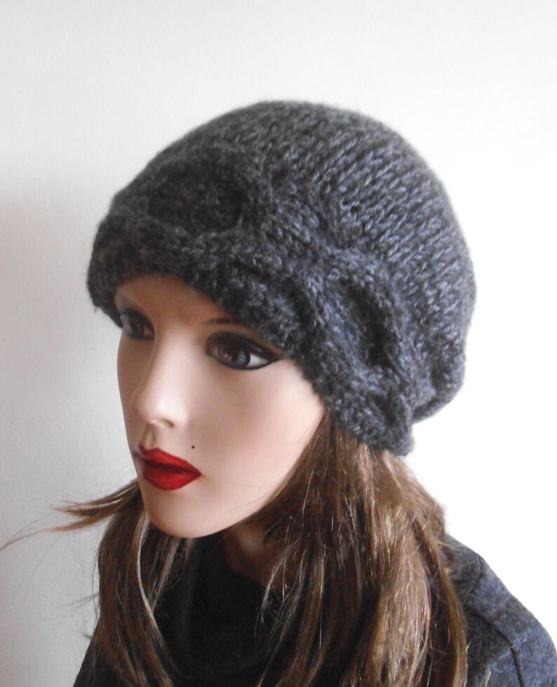 May include: A grey knitted beanie with a unique folded design. The beanie is made from a soft, textured yarn.