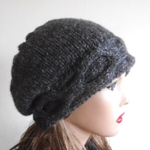 May include: A dark grey knitted beanie with a cable knit design. The beanie is slouchy and has a wide brim.