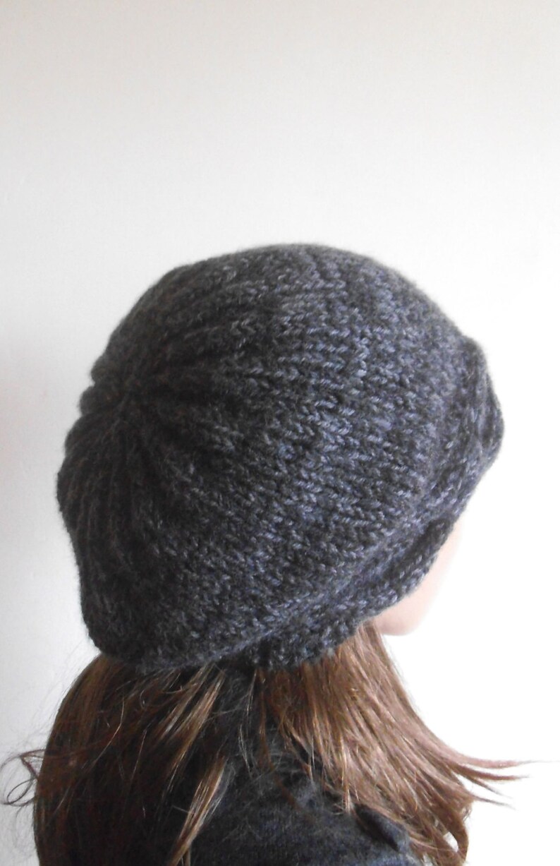 May include: A dark grey knitted beanie hat with a slouchy fit. The hat is made from a soft, textured yarn.