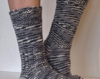 May include: A pair of gray and white knitted socks. The socks have a ribbed pattern with alternating bands of gray, black, and white. The cuffs are folded over, revealing a textured edge. The socks appear to be handmade and are designed for warmth.