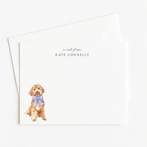 May include: A white stationery set featuring a watercolor illustration of a golden doodle dog wearing a blue gingham bow tie. The text "a note from KATE CONNELLY" is printed at the top of the card. Includes a matching envelope.