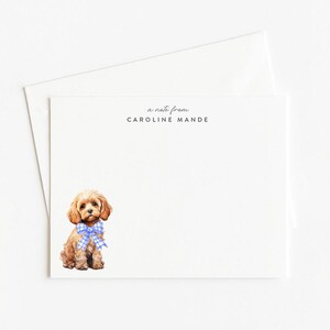 May include: A white stationery set featuring a watercolor illustration of a small, brown dog with a blue and white checkered bow tie. The text "a note from CAROLINE MANDE" is printed at the top of the card.