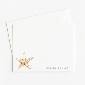 May include: White stationery set featuring a starfish illustration. The set includes a folded card and an envelope. The card has a watercolor starfish design in shades of tan and brown. The name "Helena Dunlap" is printed in black.