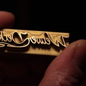 Op de afbeelding: Een close-up van een houten stempel met de woorden "Weave Deck" erin gegraveerd.