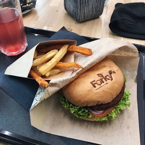 May include: A tray with a burger, fries, and a drink. The burger has a bun with the word "Forky's" on top, lettuce, tomato, and a patty. The fries are a mix of regular and sweet potato fries. A glass of pink liquid is on the left.