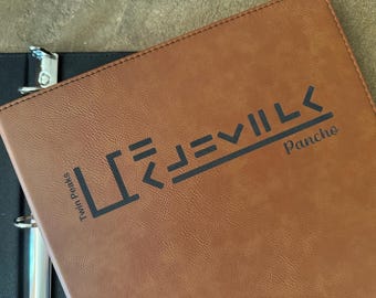 May include: Brown leather binder with black text that reads "EVIL LKS" and "Pancho". The words "Twin Peaks" are also printed on the binder. The binder is partially open, revealing a black interior and metal rings.