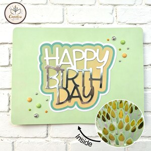 Op de afbeelding: Een lichtgroene wenskaart met de tekst HAPPY BIRTHDAY in een gelaagd ontwerp met een metallic zilveren afwerking. De kaart is versierd met kleine ronde versieringen in tinten groen en oranje. Een cirkelvormige inzet toont de binnenkant.