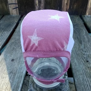 May include: A pink and white baby hat with white stars. The hat is made of a soft, stretchy fabric and has a white trim around the edge.