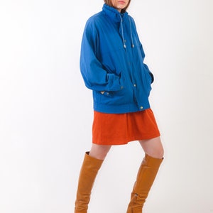 May include: A woman wearing a blue jacket, a rust-coloured mini skirt, and brown knee-high boots.