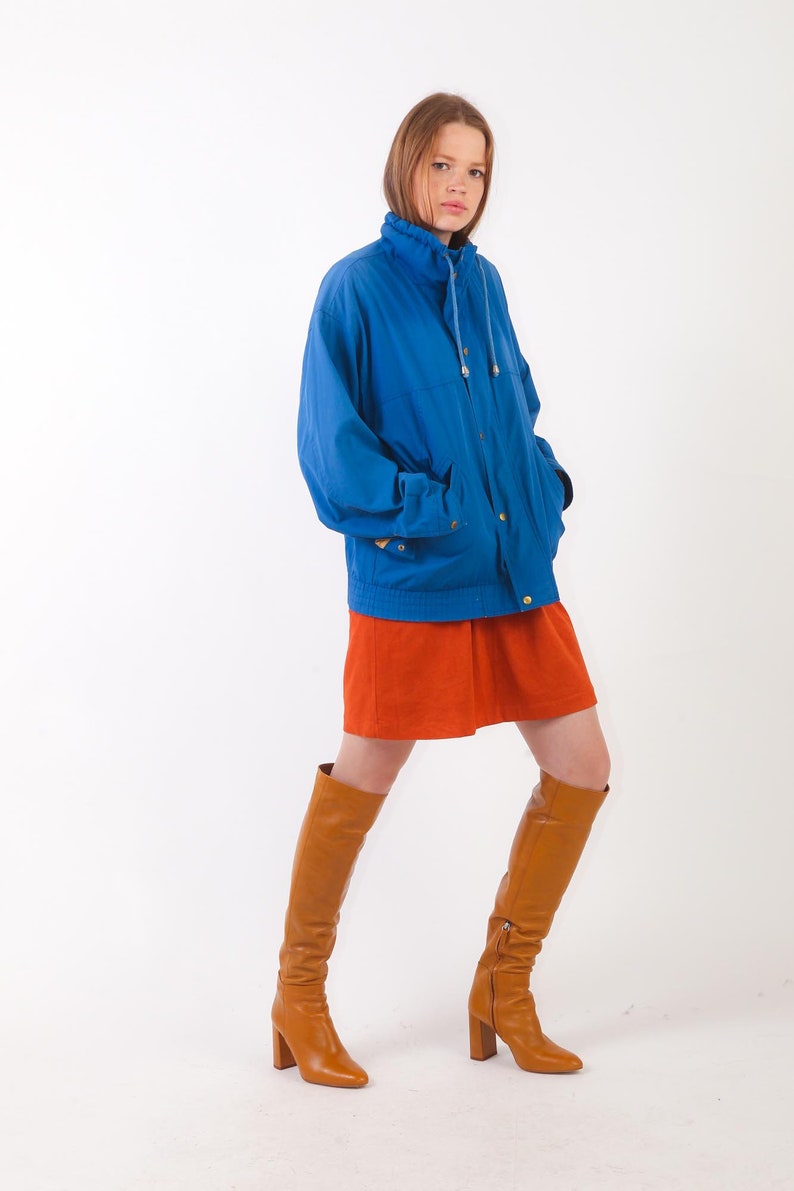 May include: A woman wearing a blue jacket, a rust-coloured mini skirt, and brown knee-high boots.