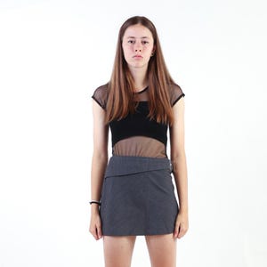 May include: A black top featuring a sheer mesh overlay with short sleeves and a solid black bodice, paired with a dark gray mini skirt that has a distinct folded waistband detail and a side buckle closure, creating a layered two-piece ensemble.