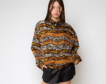 May include: A long-sleeve zip-up jacket featuring a multi-colored pattern of horizontal stripes, animal prints, and geometric motifs in shades of brown, black, yellow, and white, paired with solid black shorts with a curved hemline.