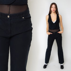 May include: A pair of black, straight-leg jeans with a button fly and belt loops. The jeans are shown on a model wearing a black vest and a white lace bralette.