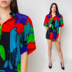 Pode incluir: Uma camisa de bot&atilde;o de manga curta com estampa abstrata em tons de vermelho, azul, verde, preto e roxo.