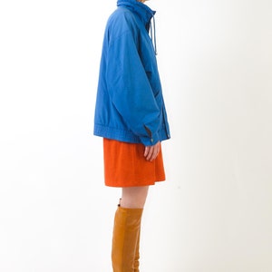 May include: A woman wearing a blue jacket, an orange skirt, and brown knee-high boots.