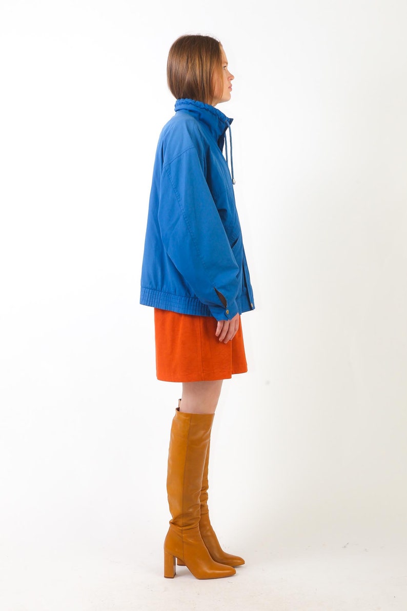 May include: A woman wearing a blue jacket, an orange skirt, and brown knee-high boots.