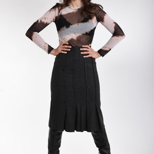May include: A long-sleeved mesh top with a brown, black, and white tie-dye pattern worn over a black camisole, paired with a dark gray midi skirt featuring vertical pleats and double-breasted buttons, and black knee-high leather boots.