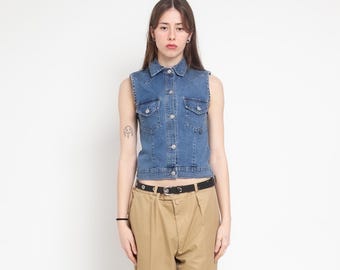 May include: A sleeveless blue denim vest featuring a classic collar, a front button-down closure with silver-toned buttons, and two chest pockets with buttoned flaps. The vest is paired with tan trousers held by a black belt with a silver buckle.