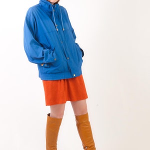 May include: A woman wearing a blue jacket, a short orange skirt, and brown knee-high boots.