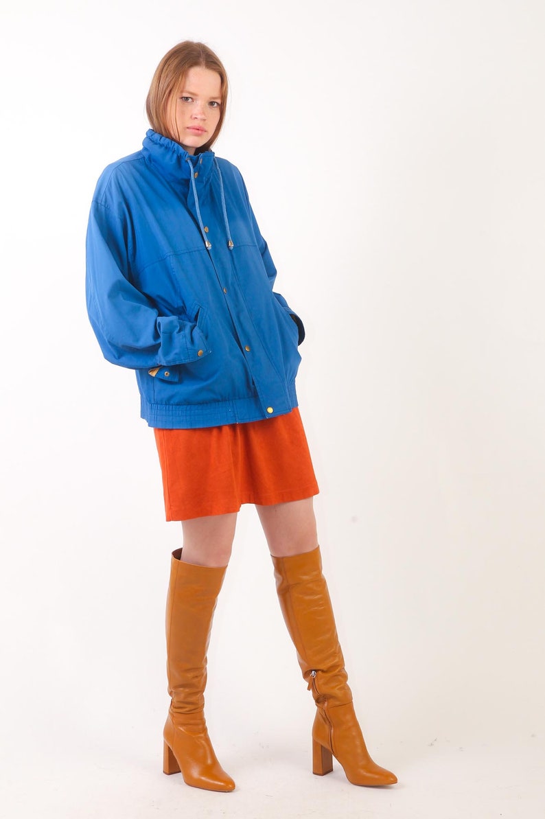 May include: A woman wearing a blue jacket, a short orange skirt, and brown knee-high boots.