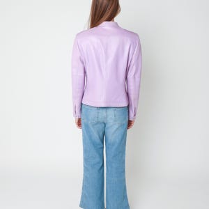 May include: A light purple leather jacket with a mandarin collar and long sleeves, paired with blue denim jeans featuring a decorative laser-cut floral pattern along the outer side seams of the legs and a straight-leg silhouette.
