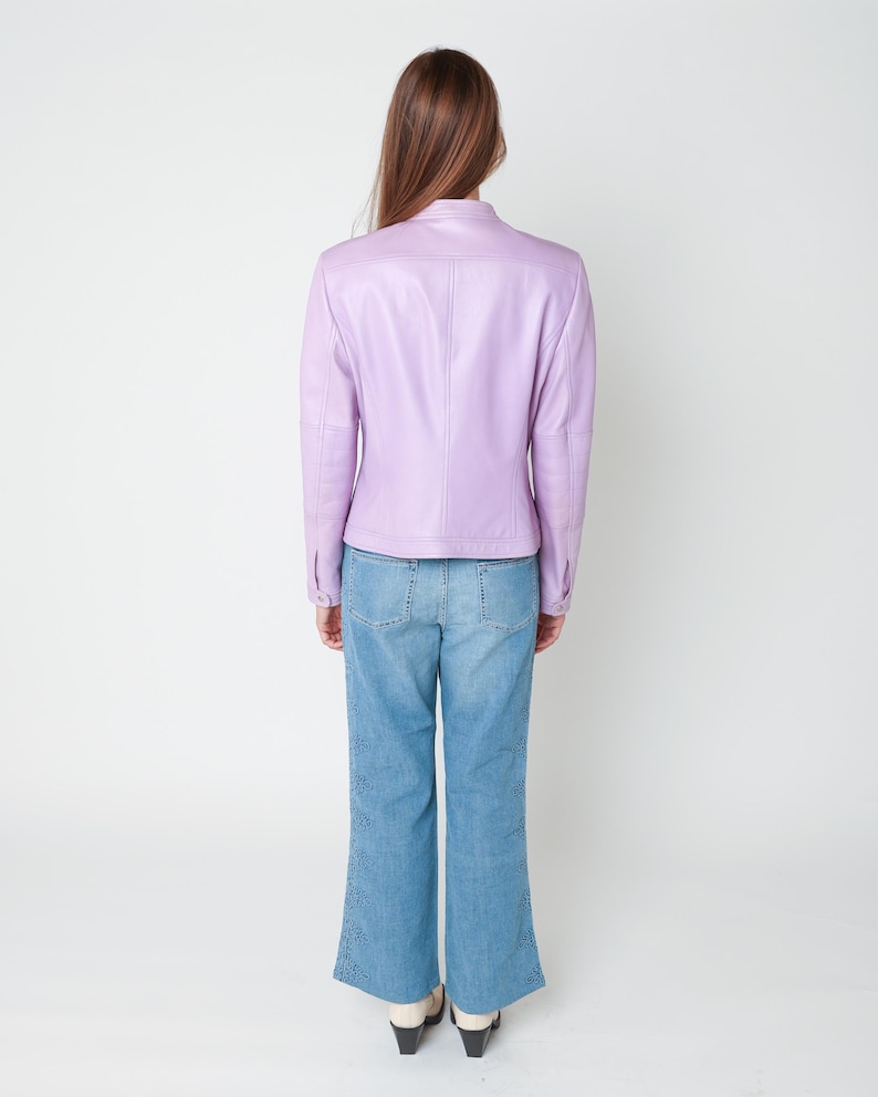 May include: A light purple leather jacket with a mandarin collar and long sleeves, paired with blue denim jeans featuring a decorative laser-cut floral pattern along the outer side seams of the legs and a straight-leg silhouette.