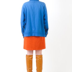 May include: A woman wearing a blue jacket, an orange skirt, and brown knee-high boots.