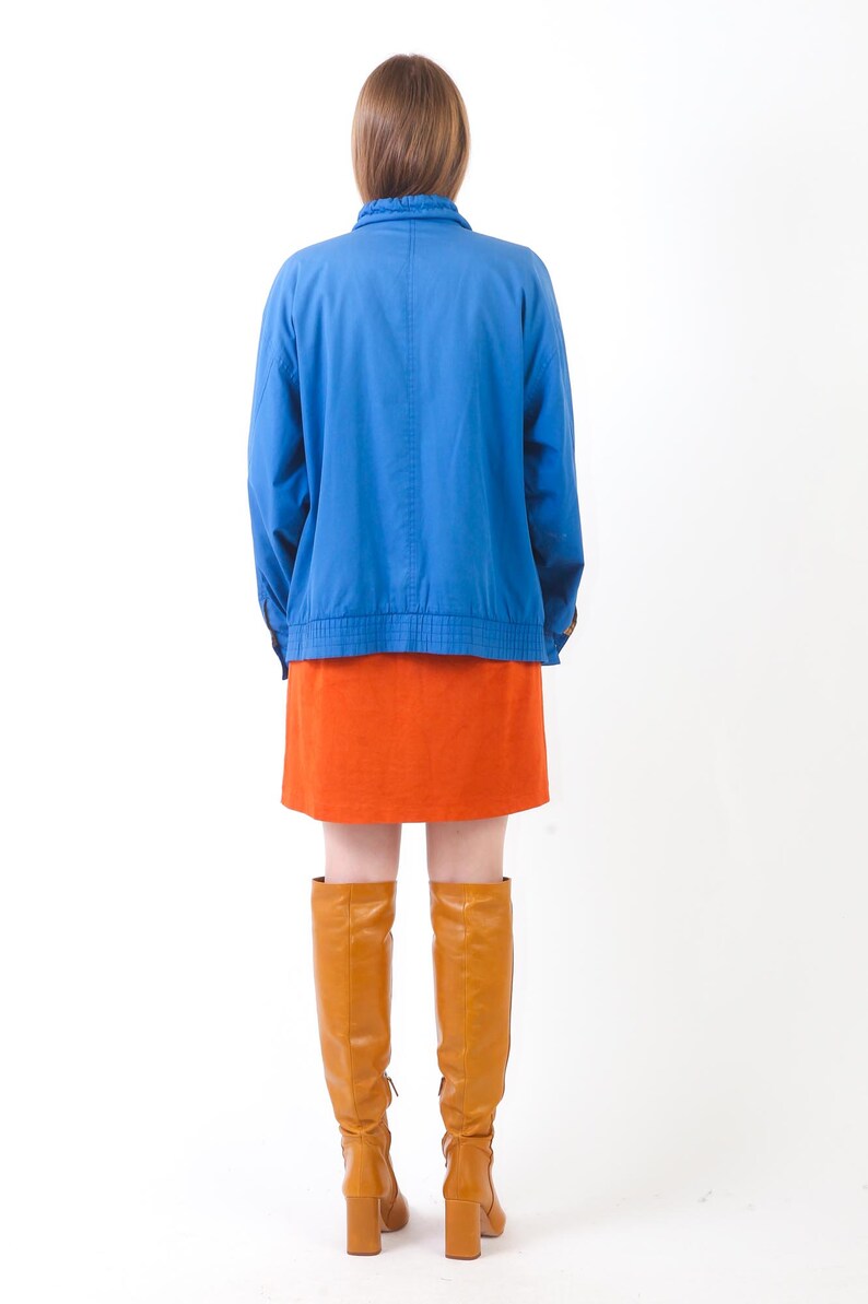 May include: A woman wearing a blue jacket, an orange skirt, and brown knee-high boots.