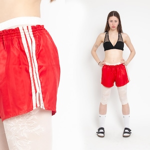May include: Red satin shorts with white stripes down the sides. The shorts have a drawstring waistband and are worn with white tights.