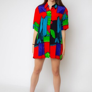 Pode incluir: Uma camisa de bot&otilde;es de manga curta com estampa abstrata em vermelho, azul, verde e preto. A camisa tem um caimento solto e &eacute; feita de um tecido leve.