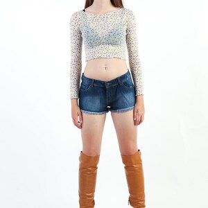 May include: A woman wearing a white floral crop top, blue denim shorts, and brown knee-high boots.