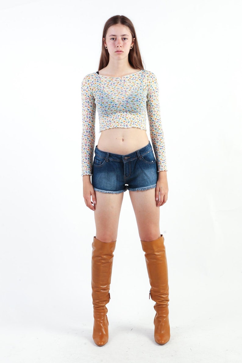 May include: A woman wearing a white floral crop top, blue denim shorts, and brown knee-high boots.