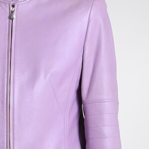 May include: A light purple leather jacket featuring a mandarin collar with a snap button closure, a full-length front zipper, and horizontal stitched detailing along the upper sleeves. The garment has a smooth finish and a fitted silhouette.