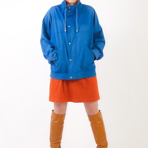 May include: A woman wearing a blue jacket with a high collar, a brown mini skirt, and brown knee-high boots.