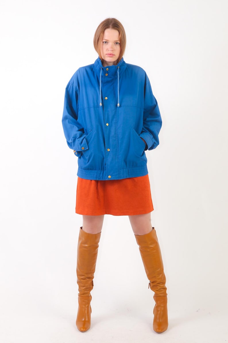 May include: A woman wearing a blue jacket with a high collar, a brown mini skirt, and brown knee-high boots.